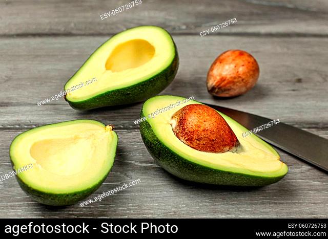 Avocado, cut in half, two seeds and chefs knife on gray wood desk