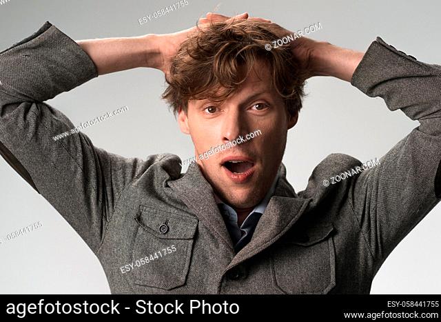 Bored young man yawns holding hands behind head. Close up portrait of male in casual wear isolated on white background
