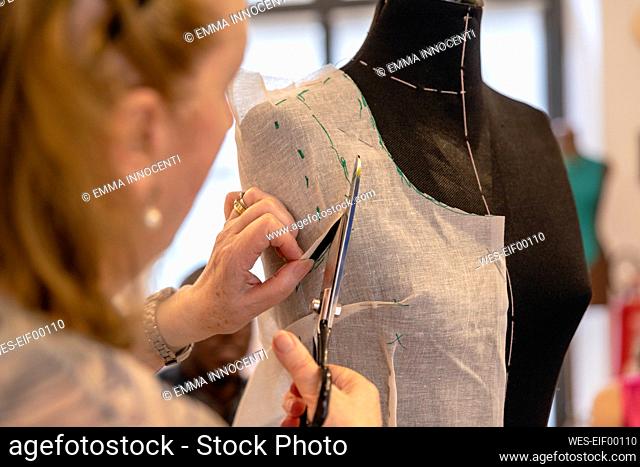 Close-up of senior designer cutting fabric on mannequin with scissors in atelier