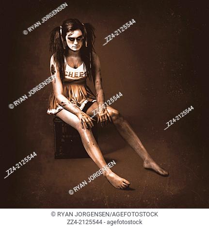 Vintage B grade horror photo of a dead zombie cheerleader girl sitting in look of grief and sadness on a milk crate in full body with cuts and wounds