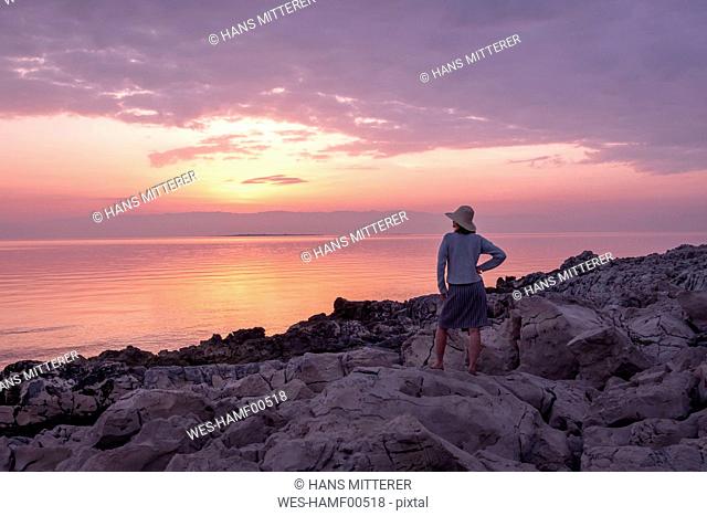 Croatia, Istria, Losinj, woman standing on rocky coast at sunset