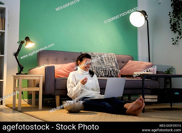 Mid adult woman using laptop while eating food sitting on floor at home