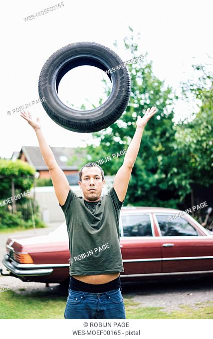 Portrait of man throwing up car tyre