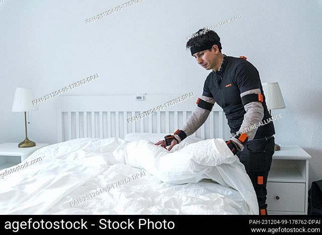 04 December 2023, Bavaria, Kulmbach: Renato Mio, a doctoral student, tidies the bed in a bedroom. He wears sensors that record his movements