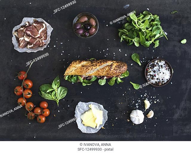 Ingredients for sandwich with smoked meat, basil, arugula, olives, cherry-tomatoes, parmesan cheese, garlic and spices