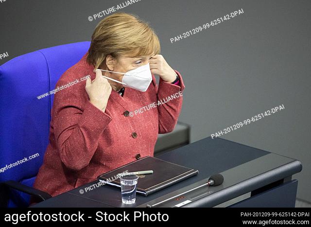 09 December 2020, Berlin: German Chancellor Angela Merkel (CDU) is removing her mouth and nose protector during the general debate on the federal budget in the...