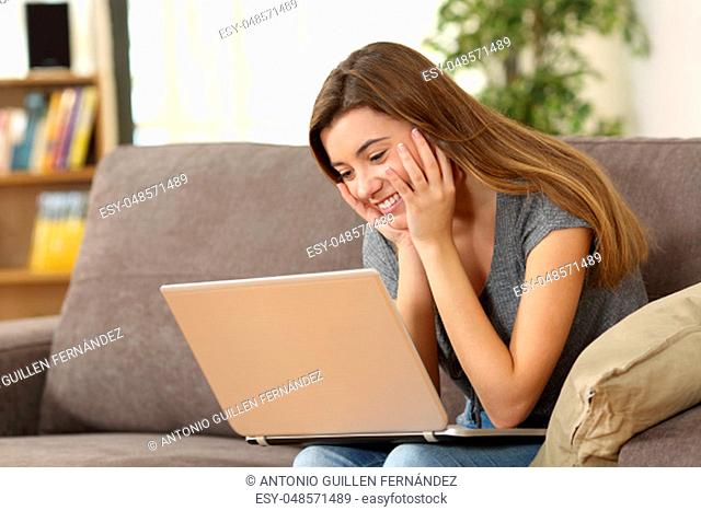 Candid girl watching media content on line in a laptop sitting on a sofa in the living room at home