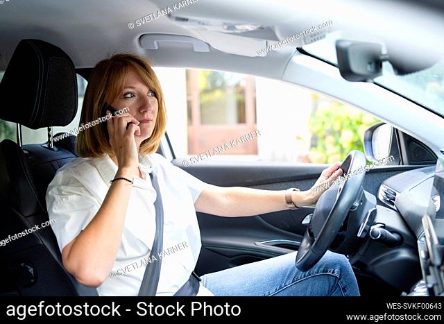 Mature woman talking through smartphone and driving car