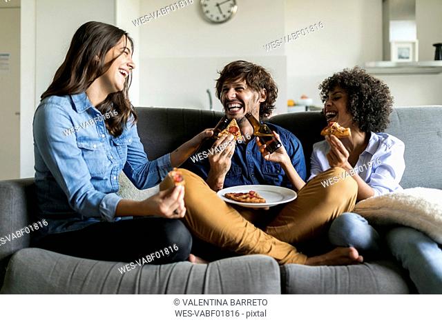 Cheerful friends sitting on couch drinking beer and eating pizza