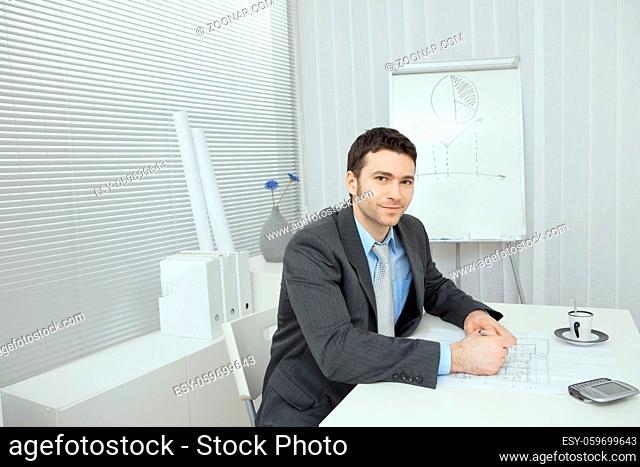 Young businessman, sitting at office desk, writing notes on floor plan
