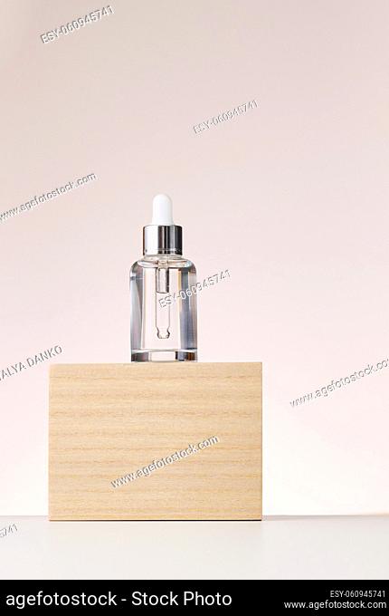 glass transparent white bottle with a pipette stands on a wooden podium. Container for cosmetics, acids and oils on a beige background