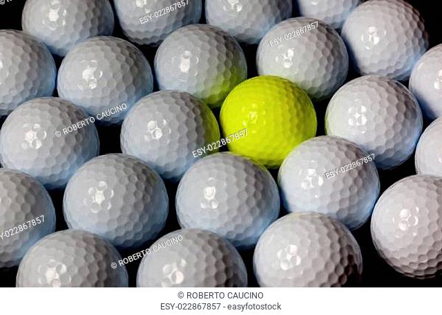Golf balls. Single yellow ball mixed within many white balls