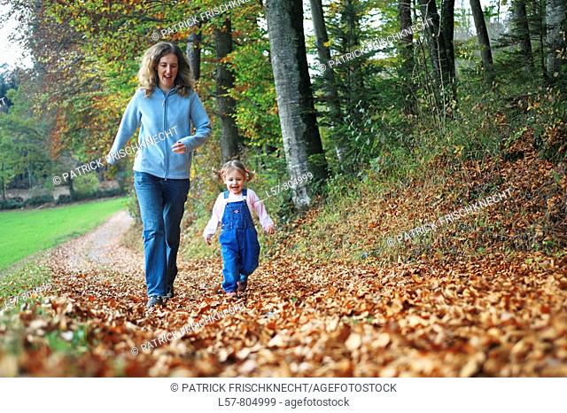 Mother with daughter running on path full of leaves in fall, having fun and laughing, autumn foliage covering path in forest, autumn, fall, Zuerich, Switzerland