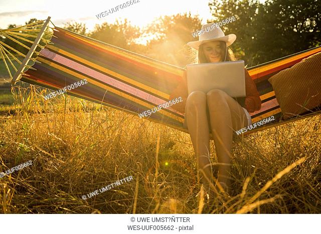 Woman wearing hat sitting in a hammock using laptop