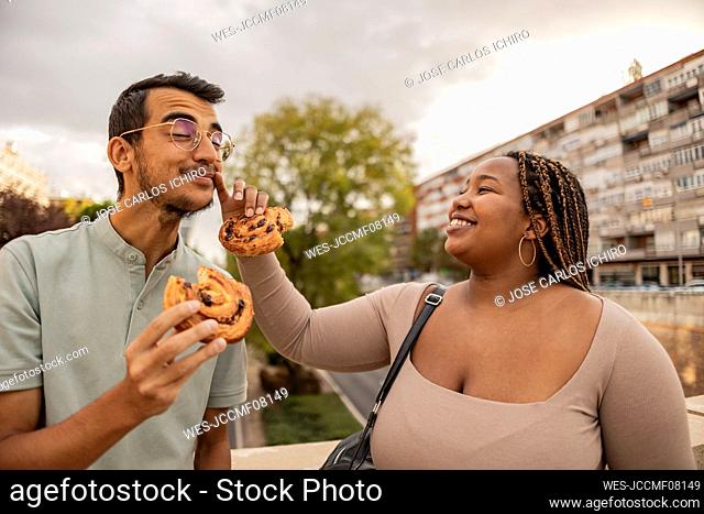 Happy young woman wiping boyfriend's face and standing with sweets under cloudy sky