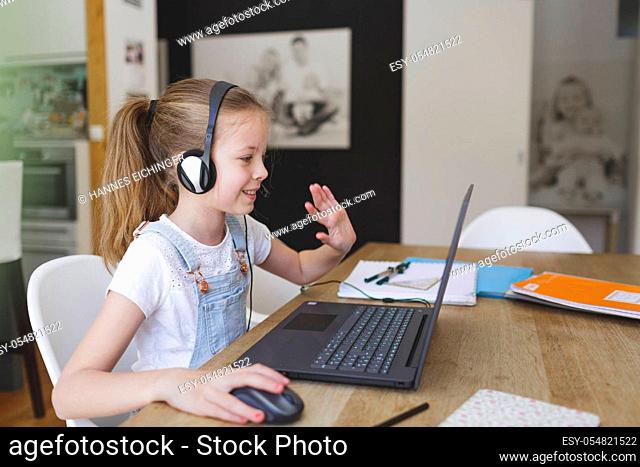 beautiful young girl with headset is sitting in front of her laptop during corona time
