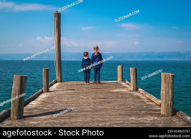 Little girl holding hands with her boy brother while standing on the wooden pier on the shore of Lake Ohrid, Northern Macedonia