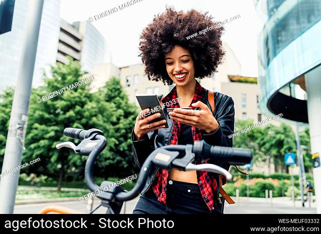 Smiling woman holding credit card while using mobile phone in city