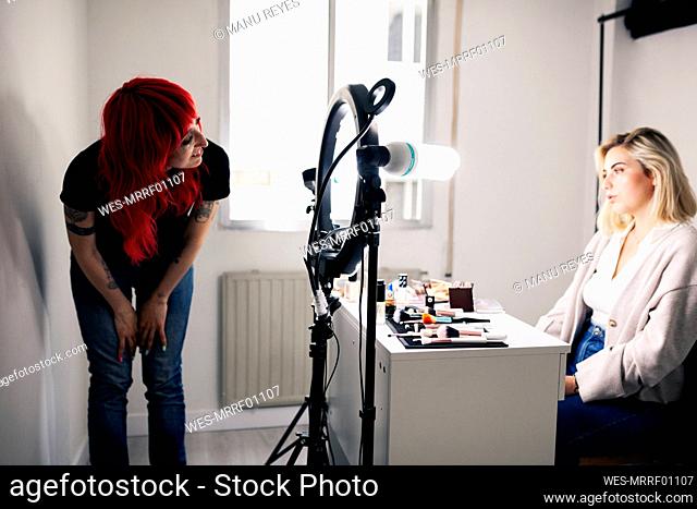 Smiling female make-up artist looking at beautiful model sitting in studio