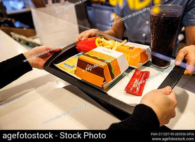 02 December 2021, Bavaria, Munich: An employee hands over a tray with French fries, a Coca Cola, ketchup and a Big Mac at a branch of the McDonald's fast food...