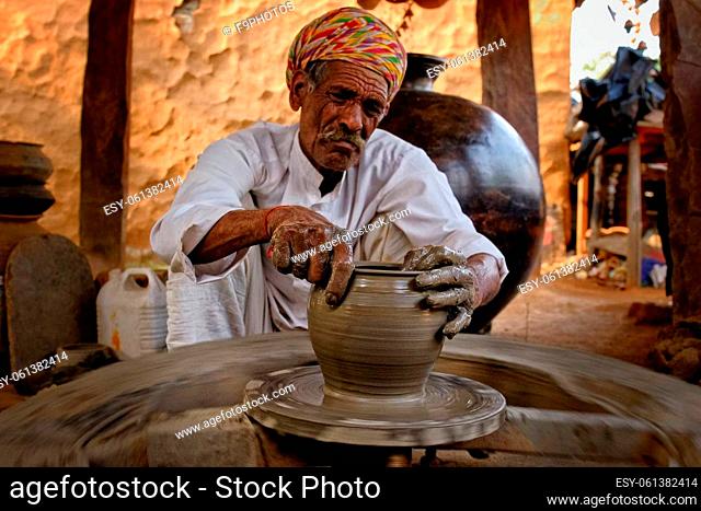 Indian potter at work: throwing the potter's wheel and shaping ceramic vessel and clay ware: pot, jar in pottery workshop. Experienced master