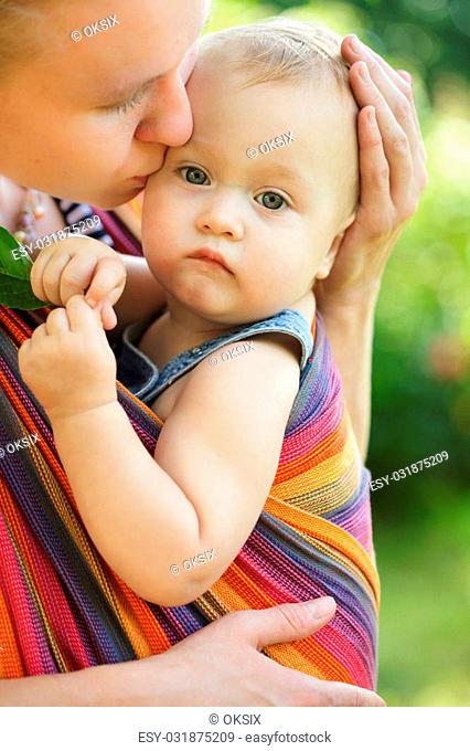 Baby in sling outdoor. Mother is carrying her child and showing nature details