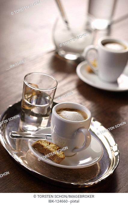 A cup of espresso macchiato with cantuccini and a glass of water