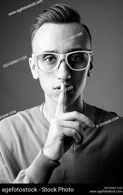 Studio shot of young handsome nerd man wearing eyeglasses against gray background in black and white