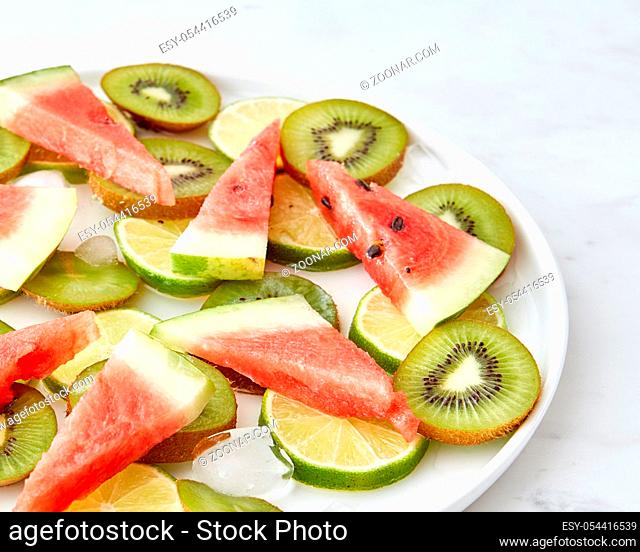 Fresh organic pieces of lime, watermelon, kiwi and melting ice cubes in a plate on a gray marble table with a copy space. Food pattern