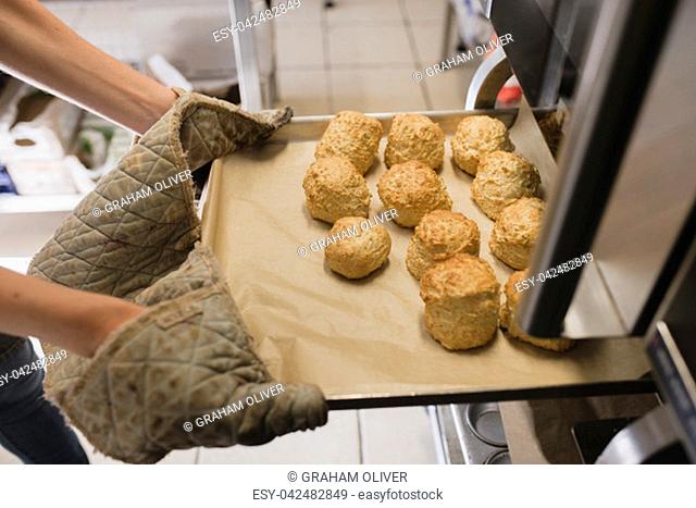 Unrecognisable person wearing oven gloves as they pull out a tray of scones from the oven