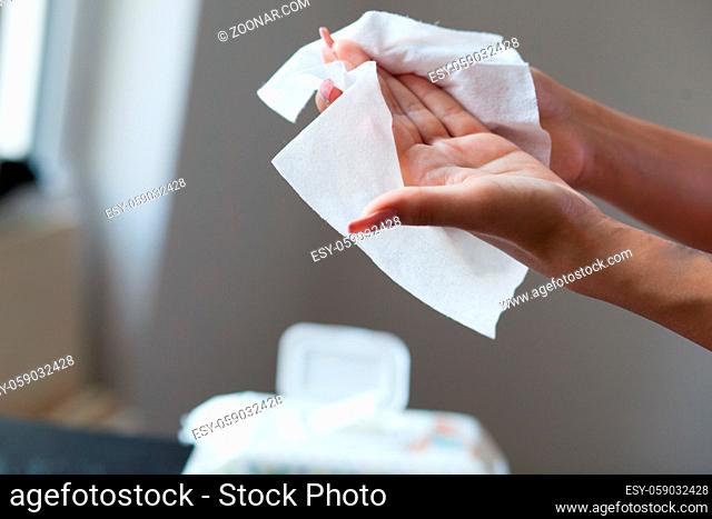 Woman with long nails clean hands with wet wipes, blurred package in background