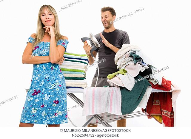 Woman very happy with her arms folded behind her a sweaty man with hysterical expression controls the temperature of the iron as many clothes ironing required