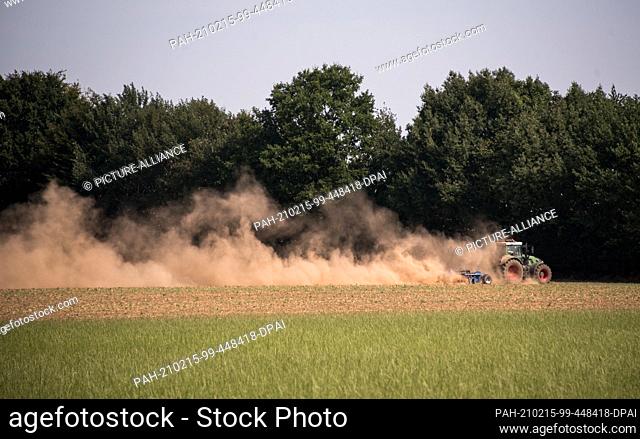 12 August 2020, Schleswig-Holstein, Hohenhorn: A farmer is working a field with the help of a tractor and a disc harrow, causing a large cloud of dust
