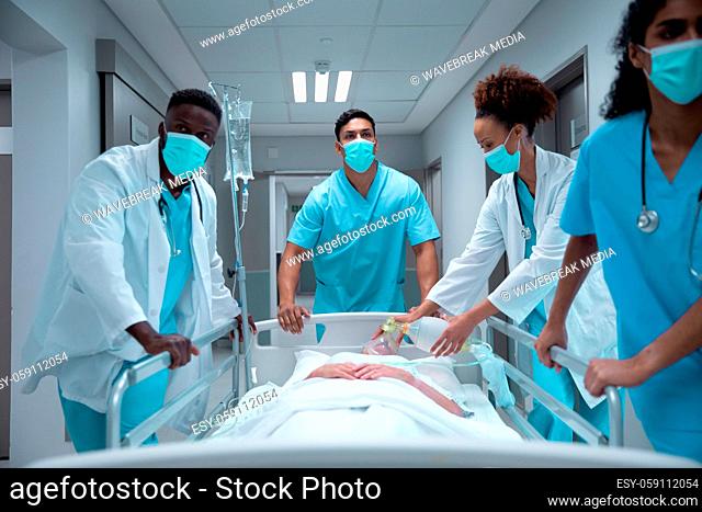 Mixed race doctors wearing face masks transporting patient in hospital bed