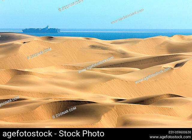Sand dune desert meets water of the Atlantic Ozean. Container ship on the water