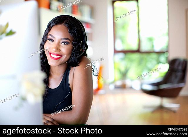 Happy young woman with headset working from home at computer