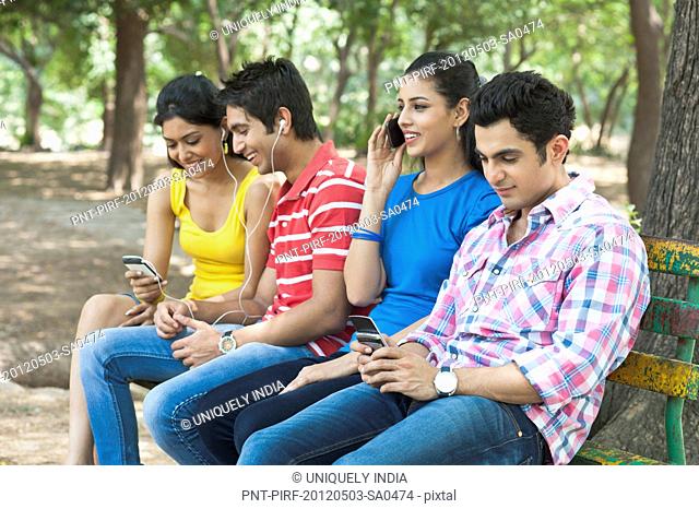 Friends using mobile phones and mp3 player in a park, Lodi Gardens, New Delhi, Delhi, India