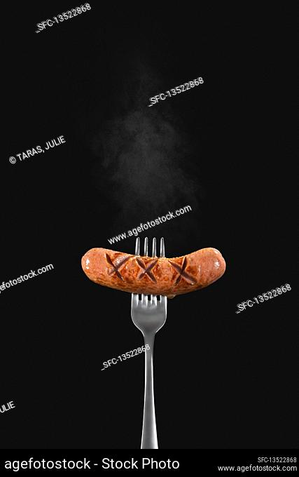 A hot sausage on a fork against a black background