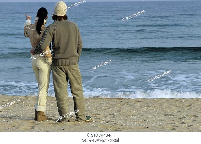 Young auburn-haired Man holding a brownhaired young Woman to his Arm - Love - Togetherness - Beach