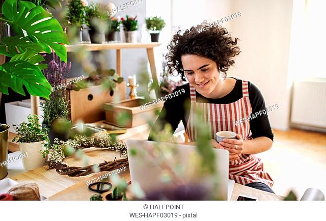 Smiling young woman using laptop in a small shop with plants