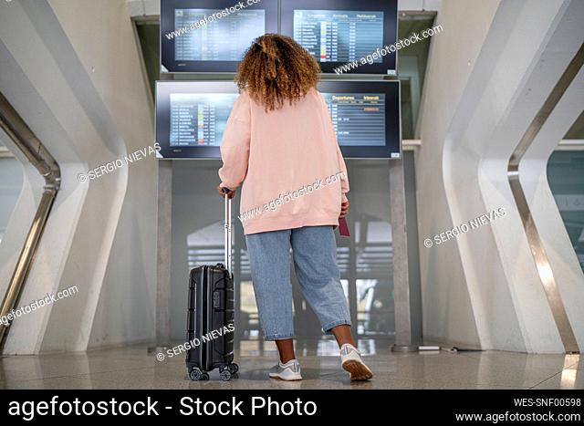 Young woman checking for flight schedule on time board at airport