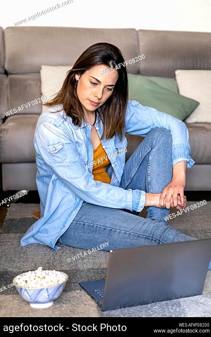 Thoughtful woman looking at laptop while sitting on carpet in living room