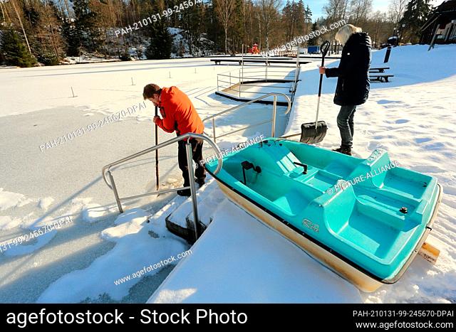 31 January 2021, Saxony-Anhalt, Hasselfelde: A helper hacks a hole in the ice in the Waldseebad with a shovel from a pedal boat