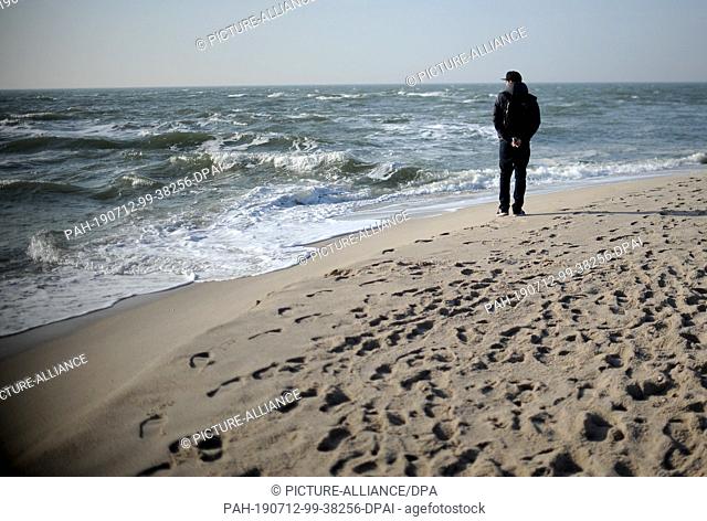 19 February 2019, Schleswig-Holstein, Sylt: A young man walks along the beach and overlooks the sea. Sylt is the largest North Frisian island in Germany