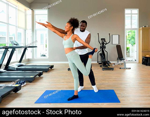 Short curly black hair coach with moustache and beard teach young woman in sportswear how to do lord of the dance yoga pose