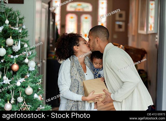 Affectionate couple with baby daughter kissing at Christmas tree