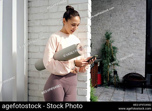 Mid adult woman with yoga mat using mobile phone on terrace