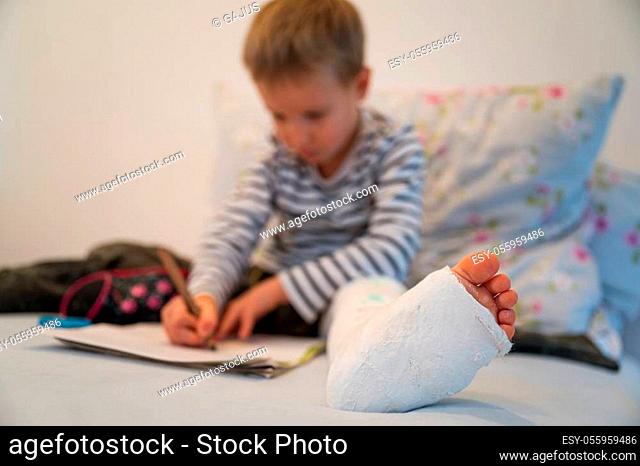 Low angle view of a toddler boy wearing plaster on his leg, drawing with color pencils