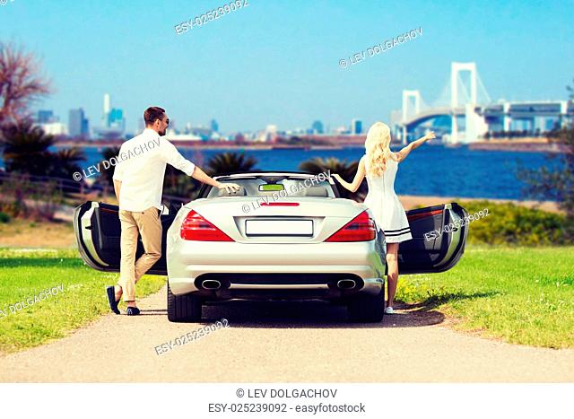 people, travel, tourism and road trip concept - happy man and woman near cabriolet car over river and tokyo rainbow bridge background