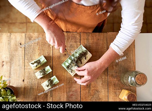 Woman cutting pieces of organic handmade soap on cutting board at workshop